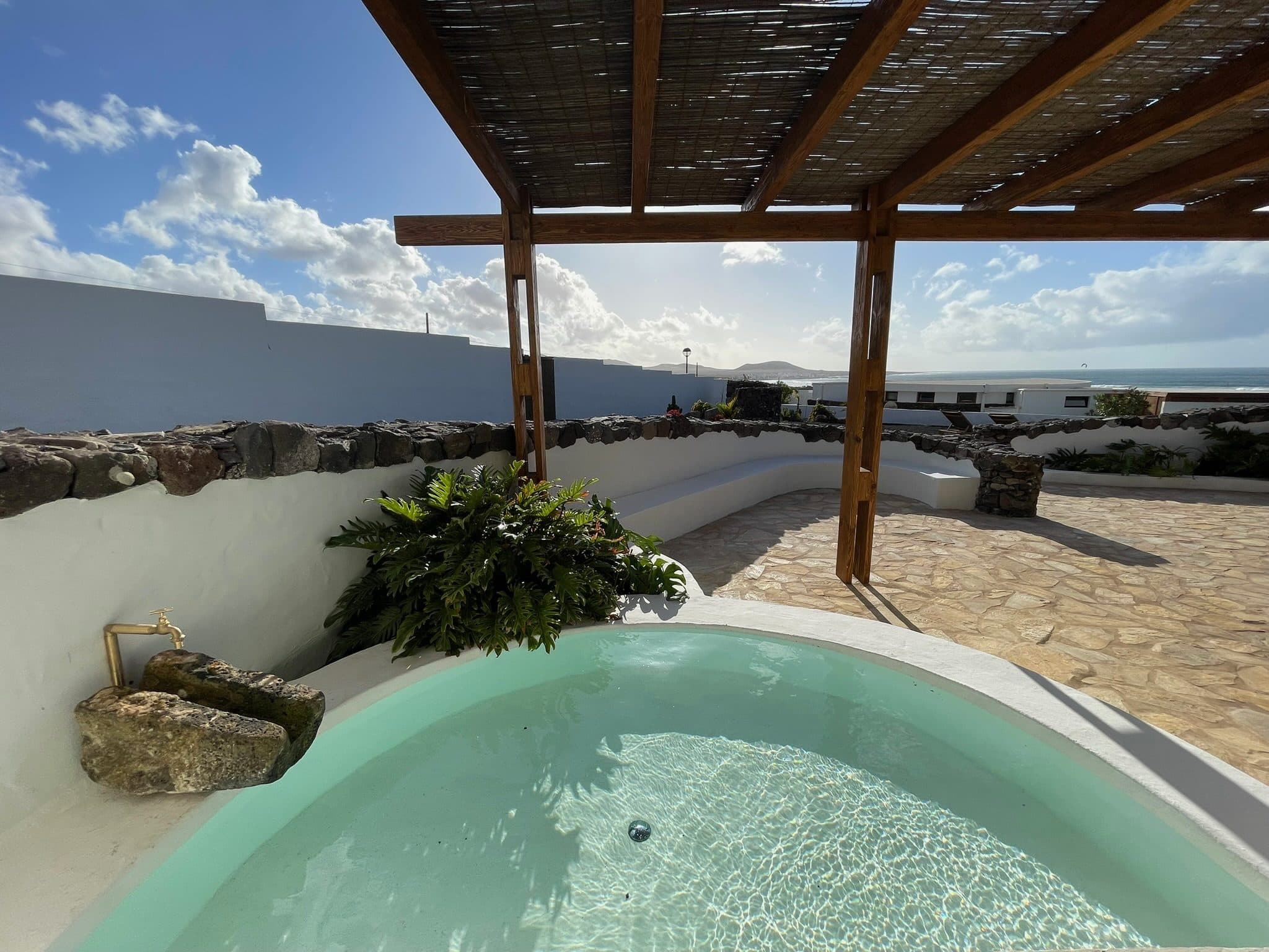A small plunge pool under a reed-roofed pergola, with the ocean on the horizon.