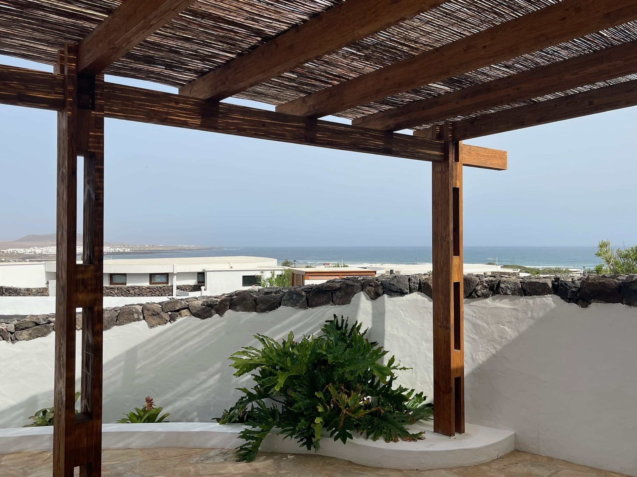 The terrace pergola framing the Atlantic beyond a white wall capped with black volcanic stone.